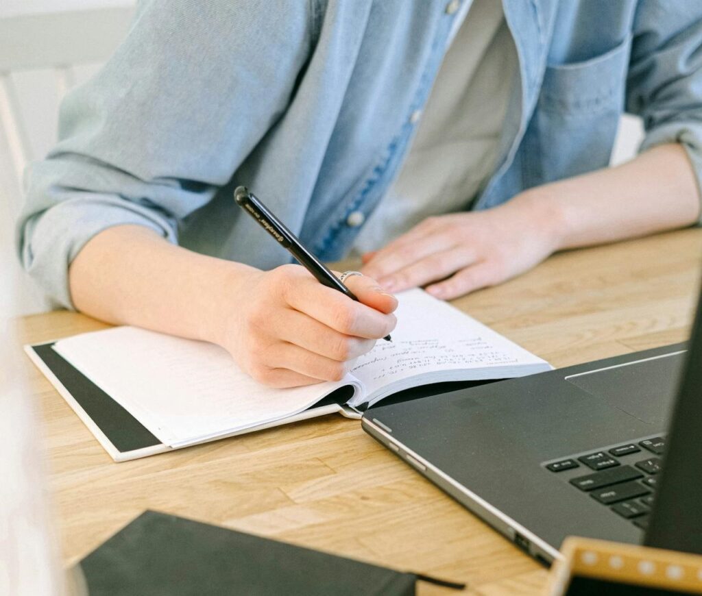 Person writing in a notebook in front of a computer.